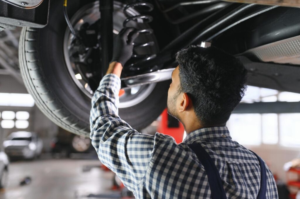 Mechanic inspecting a car shock absorber and suspension system while the vehicle is raised on a hydraulic lift in an automotive workshop