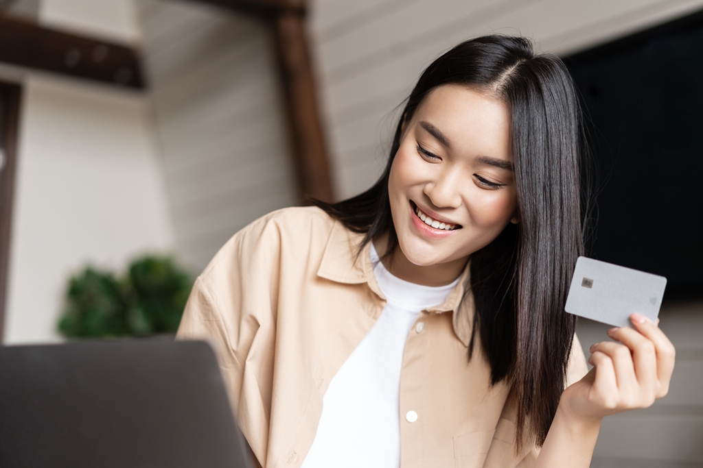 Smiling woman holding a credit card while looking at her laptop