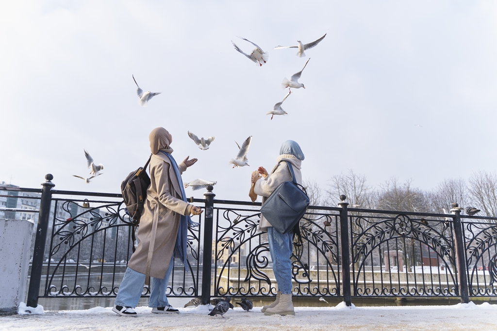Two Muslim women with hijab looking at pigeons while traveling