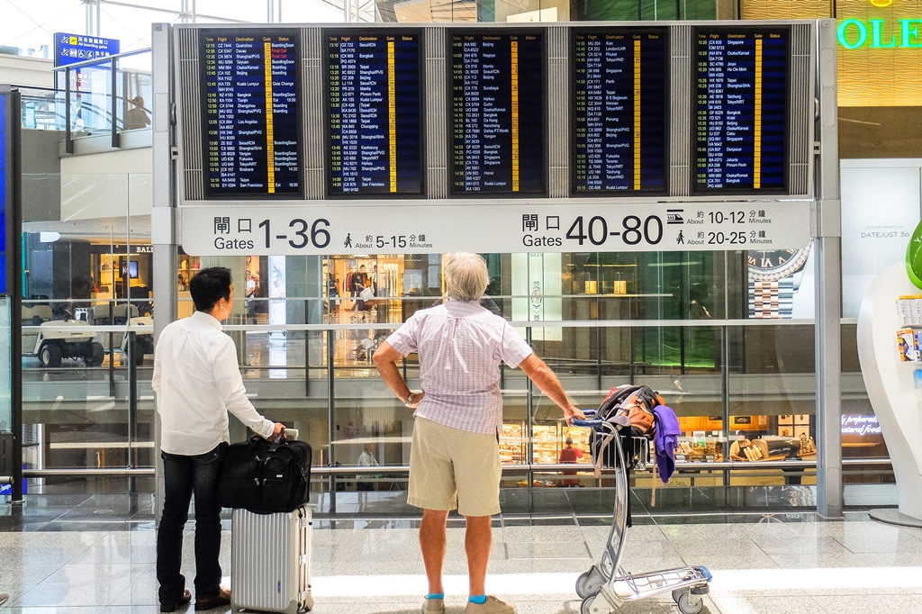 Two men standing at an airport looking at their flight status