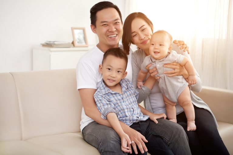 Loving Asian couple posing on a couch at home with their young son and baby.