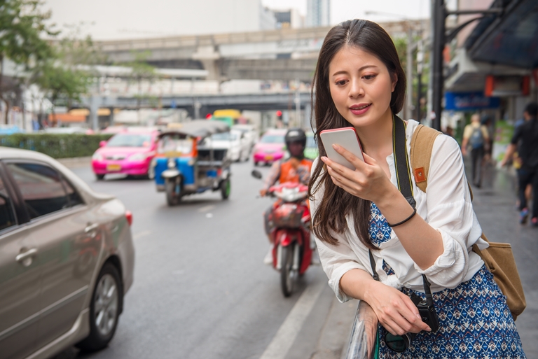 Asian female traveller by the road holding a mobile phone