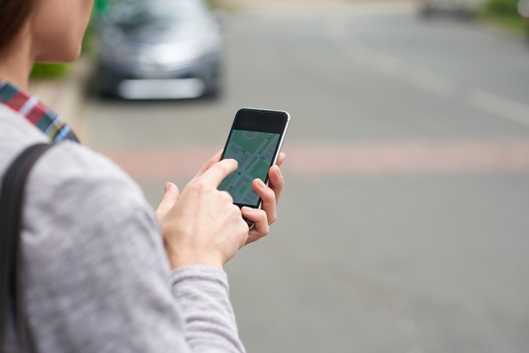 Over-the-shoulder view of an unrecognisable person tracking ride-hailing in Thailand via a mobile app